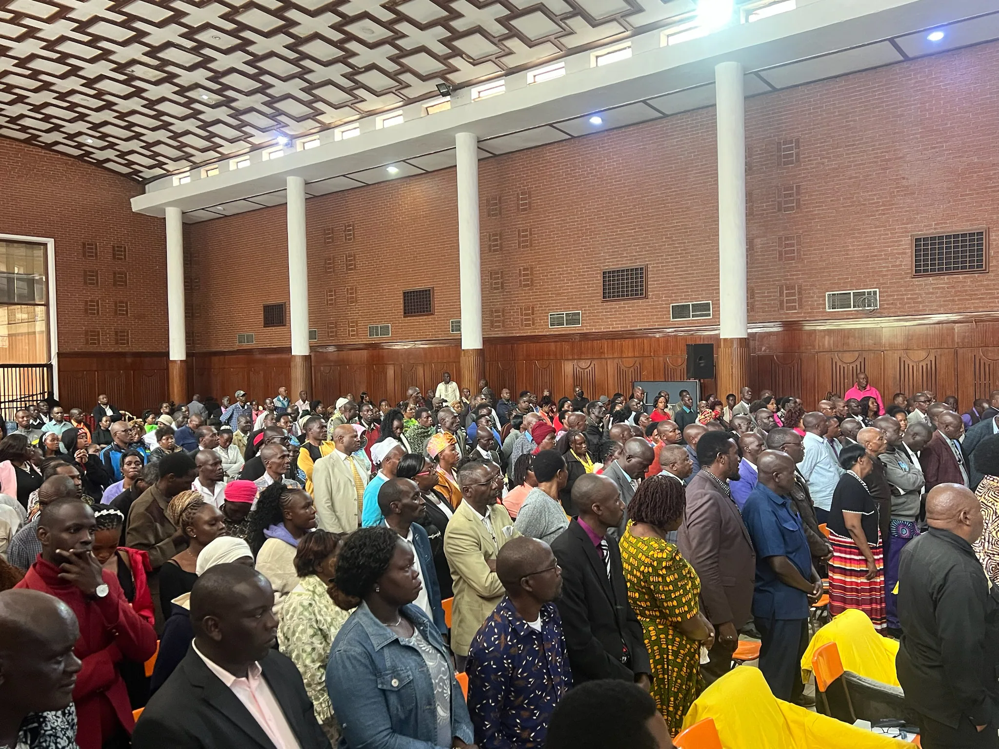 A large gathering of pastors and ministry leaders stands closely together inside Charter Hall.
